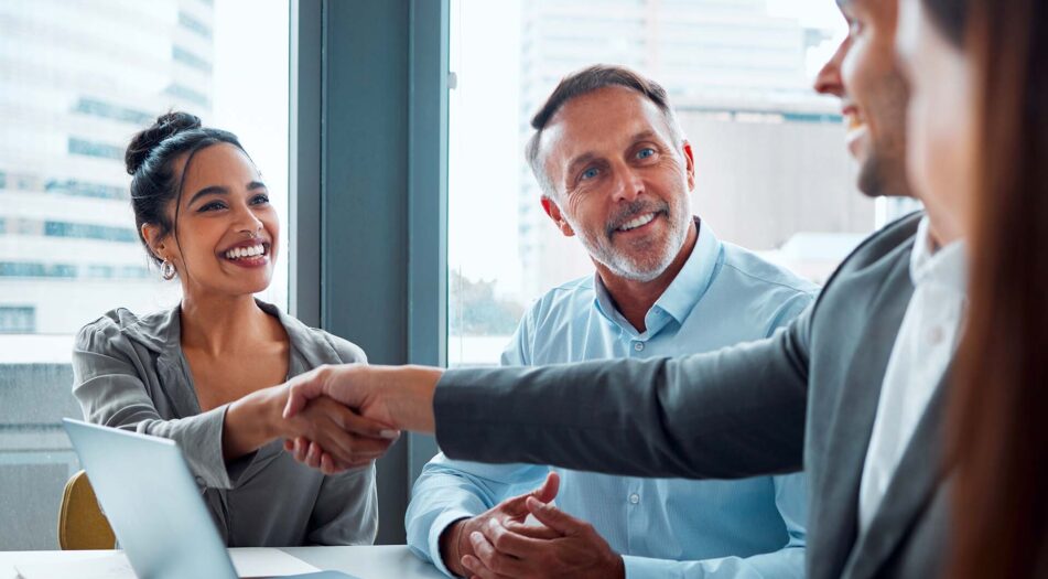 Three people seated at a table in an office with large windows overlooking a cityscape.