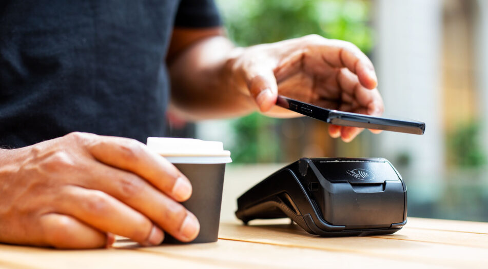 Someone paying with their phone and holding a coffee.