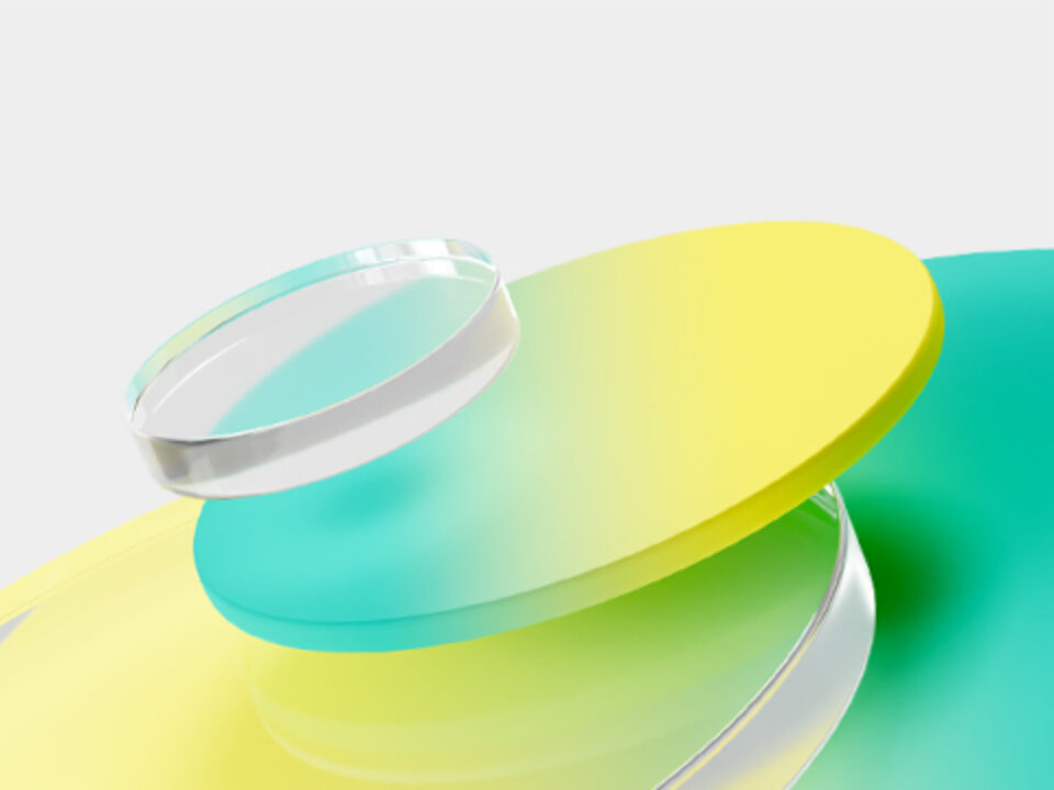 A stack of translucent, circular discs in yellow, green, and blue, topped with a clear cylindrical object, set against a light gray background